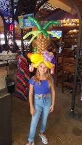 Girl at Chevy's Miami with her Carmen Miranda balloon hat. The hat contains a pineapple lots of grapes, and apple, earrings, and an orange made from balloons.